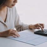 Femme assise a un bureau calculant ses allocations sur un formulaire papier avec une calculatrice