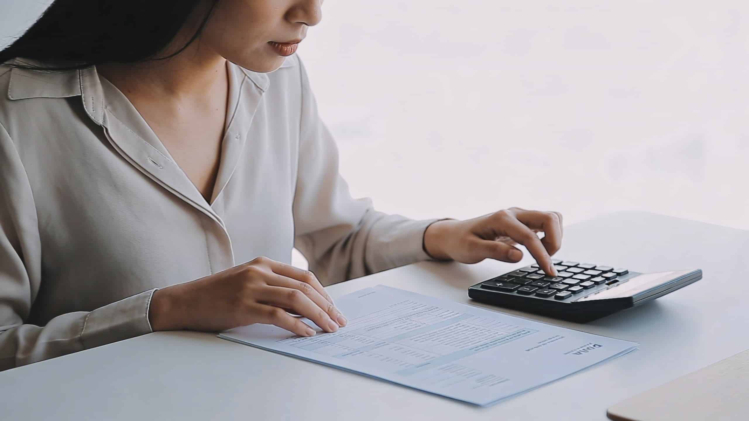 Femme assise a un bureau calculant ses allocations sur un formulaire papier avec une calculatrice