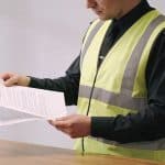 employe en gilet de securite regarde contrat partiel sur bureau