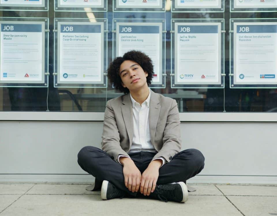 jeune adulte assis au sol devant vitrine emploi