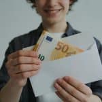 jeune adulte souriant recevant enveloppe de billets euros