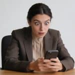 femme assise au bureau regardant smartphone intriguée