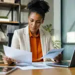 Personne assise consultant des documents financiers sur bureau avec ordinateur portable