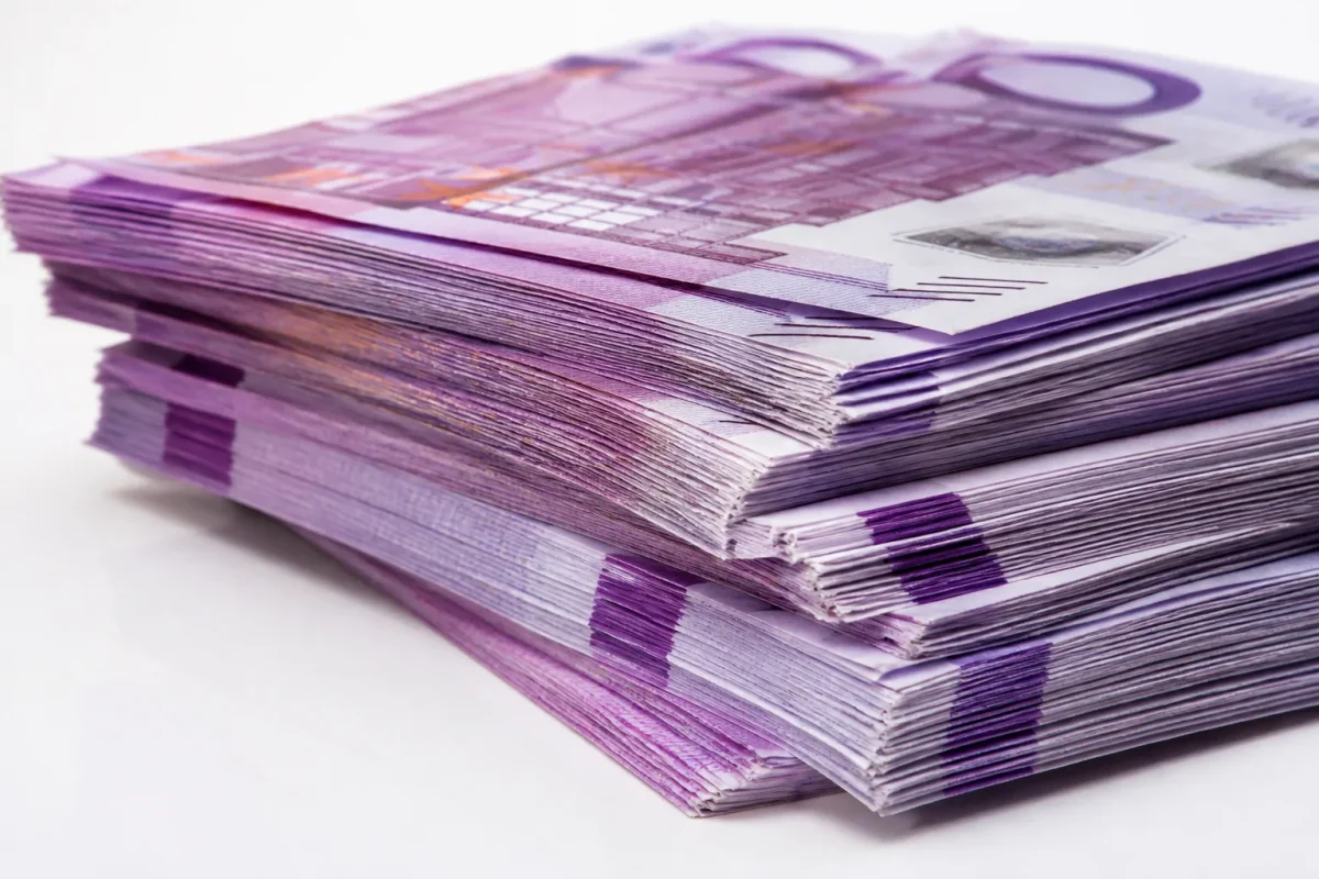 Billets de cinq cents euros empilés sur surface blanche.