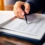 Document notarié ouvert avec stylo pointant sur chiffres financiers détaillés