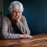 Femme agee assise seule a table vide sans argent devant elle
