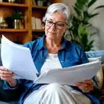 Personne agee assise tenant documents financiers entre ses mains