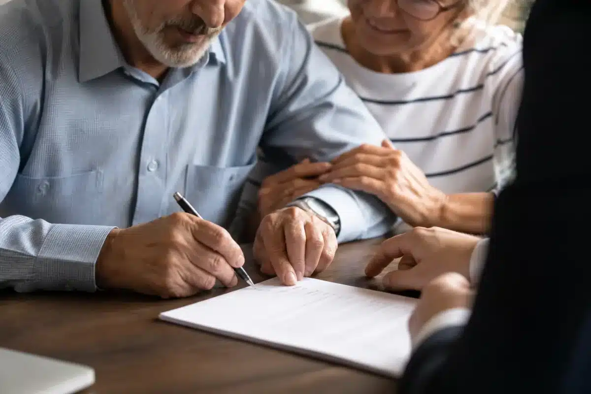 Mains âgées signant document avec conseiller professionnel présent