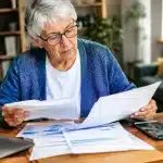 Personne agee tenant factures et relevés bancaires sur table