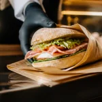 Employe en uniforme tend un sandwich au client