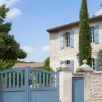 Grande maison en pierre avec volets bleus et portail