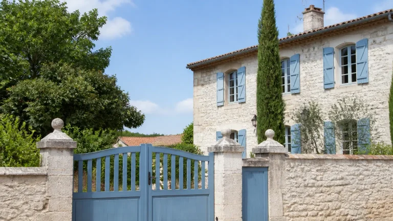 Grande maison en pierre avec volets bleus et portail