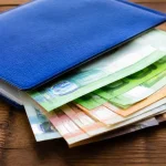Main tenant livret bleu posé sur billets empilés