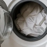Main ouvrant un lave-linge rempli de linge blanc