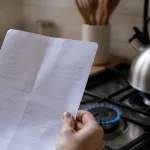 Main tenant une facture de gaz devant une cuisiniere