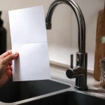 Main tenant une facture papier pres du robinet