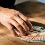Main tendant des billets sur une table en bois