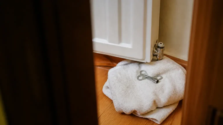 Plombier agenouille purge un radiateur avec une cle