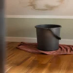 Seau posé sur parquet sous plafond tache d'humidite