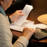 Senior assis a table avec calculatrice et releve papier
