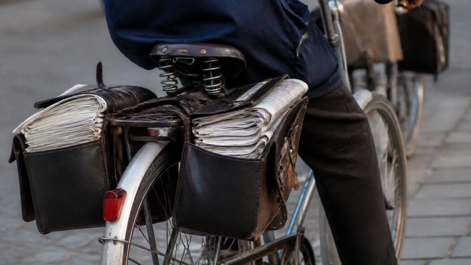 Deux seniors a velo, sacoches pleines de journaux